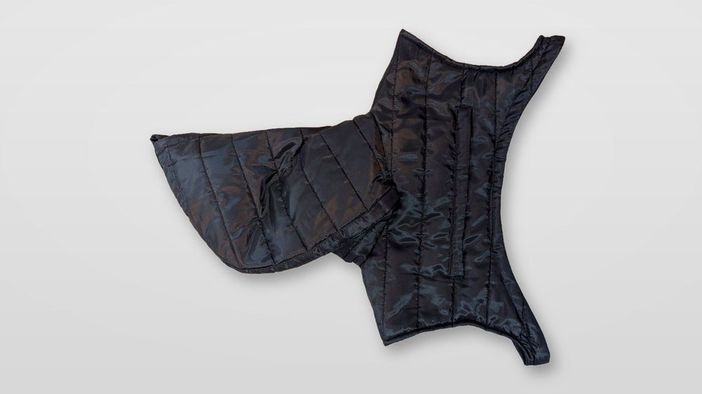 A quilted black panel of the Nova jacket laid flat on a pearl-grey surface