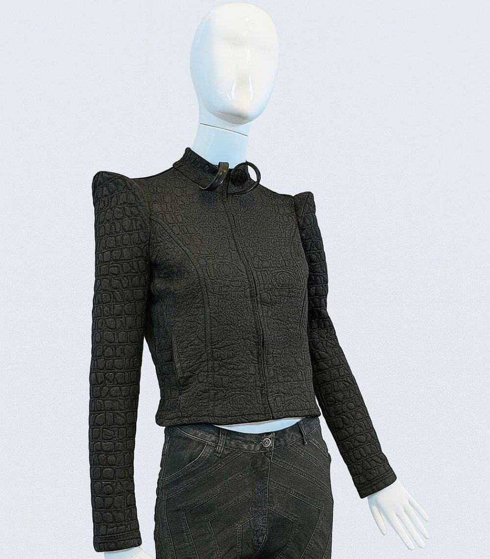 Urban Aegis Jacket — black futuristic textured cropped jacket on a mannequin, framed just below the sleeve cuffs